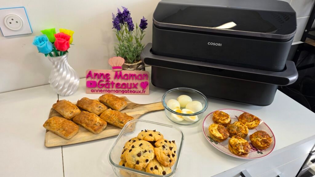 photographie de 4 recettes réalisées à l'airfryer : au premier plan, des cookies aux pépites de chocolat et 6 mini quiches sans pâte, au second plan : 6 cakes au thon individuels et 4 œufs cuit dur, pour terminer au fond l'airfryer Twinfry de COSORI, des fleurs de lavandes en pot, des roses flashy imprimées en 3D et le logo ANNE MAMAN GÄTEAUX.