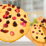 Deux maxi cookies cœurs au fruits, un entier à gauche et un coupé en deux à droite. Ils sont parsemés de fruits rouges lyophilisés et la découpe laisse apparaitre un centre fruités rempli de cerises et de fraises émincées.