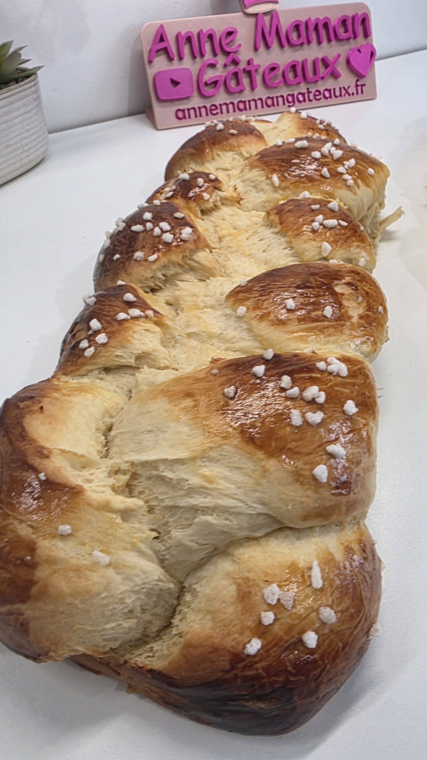 brioche tressée à la mie filante avec en fond le logo Anne Maman Gâteaux