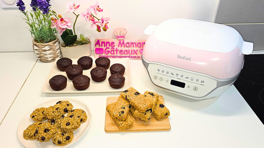 Cookies bananes, flocons d'avoine, barres énergétiques et moelleux au chocolat healthy au 1er plan, à droite l'appareil Cake Factory Infinity de Tefal et au fond logo : Anne Maman Gâteaux ainsi que deux pots de fleurs artificielles orchidées et lavande.