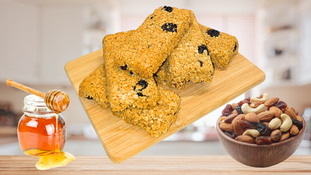 Gros plan sur 6 barres énergétiques aux flocons d'avoine avec raisins secs visibles et à gauche un pot de miel qui coule, à droite un bol de mélange d'oléagineux avec raisins secs. Arrière plan cuisine floue