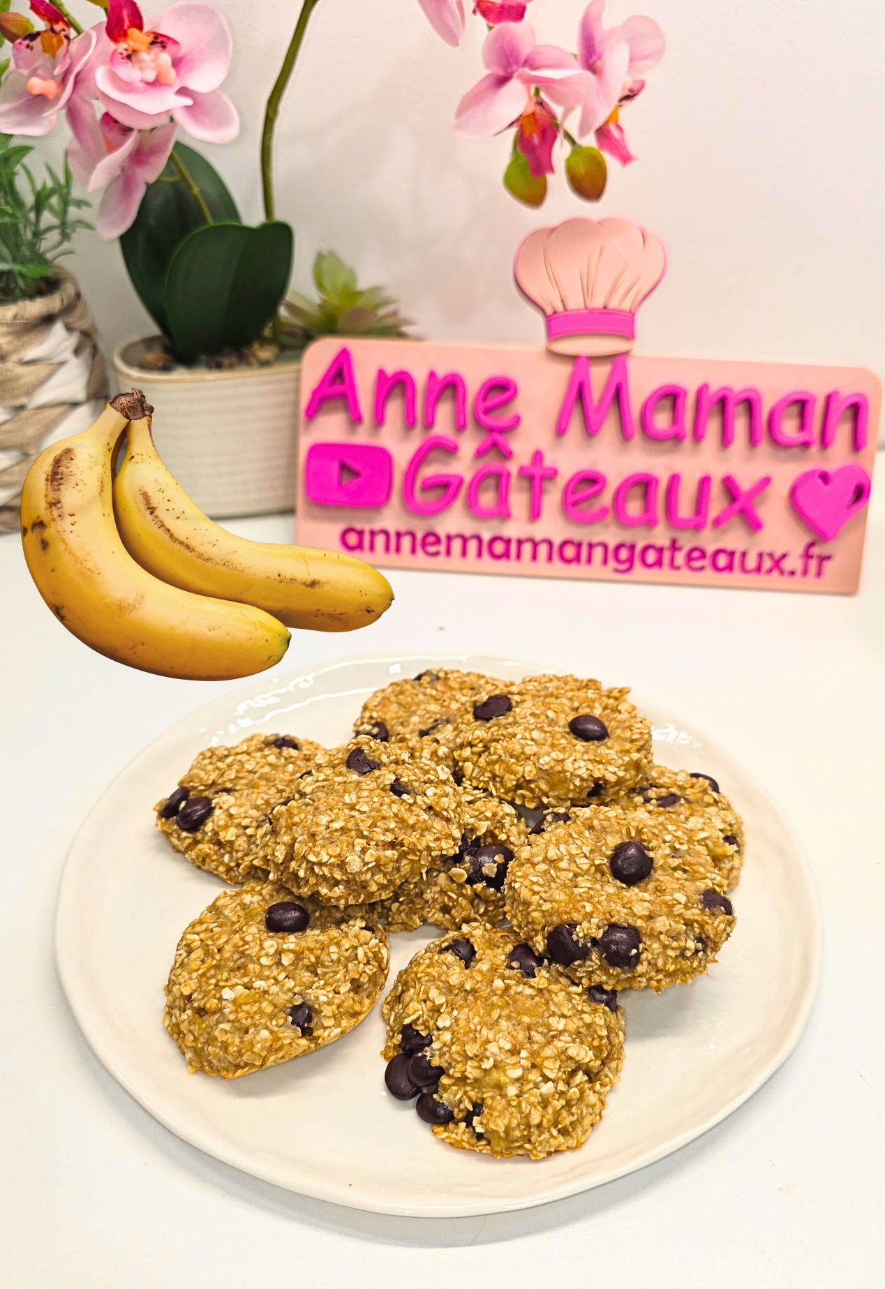 9 cookies healthy aux bananes, flocons d'avoine et pépites de chocolat au xylitol sur une assiette blanche avec deux bananes à gauche et le logo : Anne Maman Gâteaux en fond