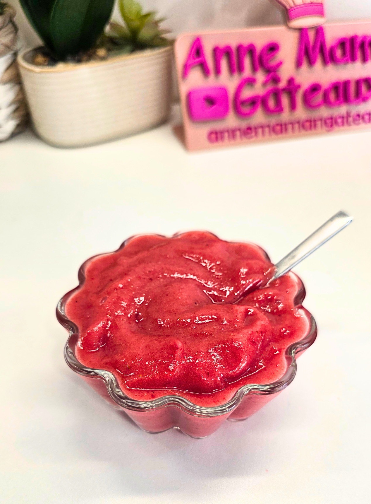 coupe de sorbet rose vif aux fraises et à la banane réalisée au Blender avec une cuillère en inox brillante plongée dedans