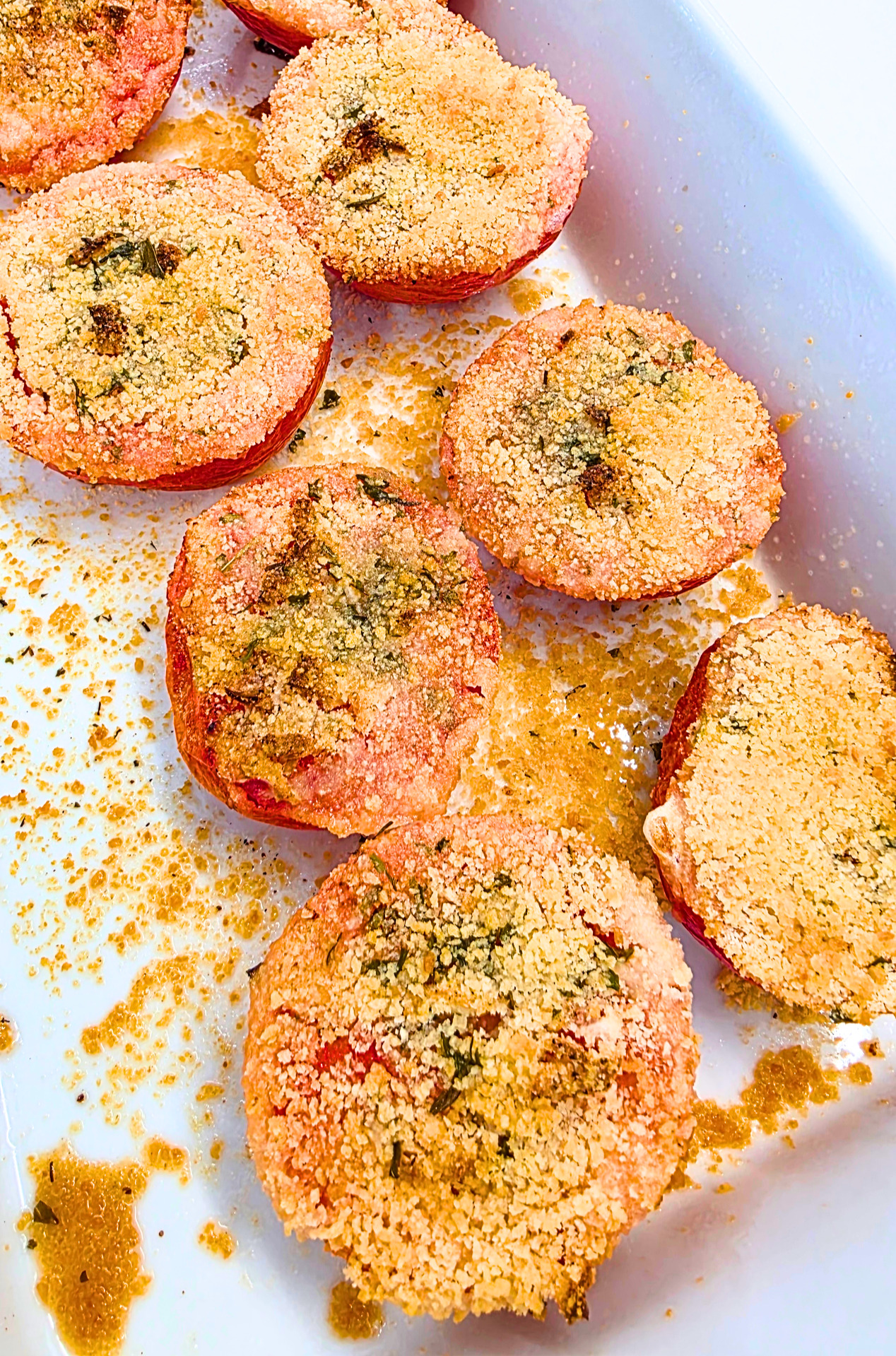 tomates à la provençale (coupées en deux, saupoudrées d'ail, sel, poivre, persil, chapelure et huile d'olive) dans un plat en céramique blanc